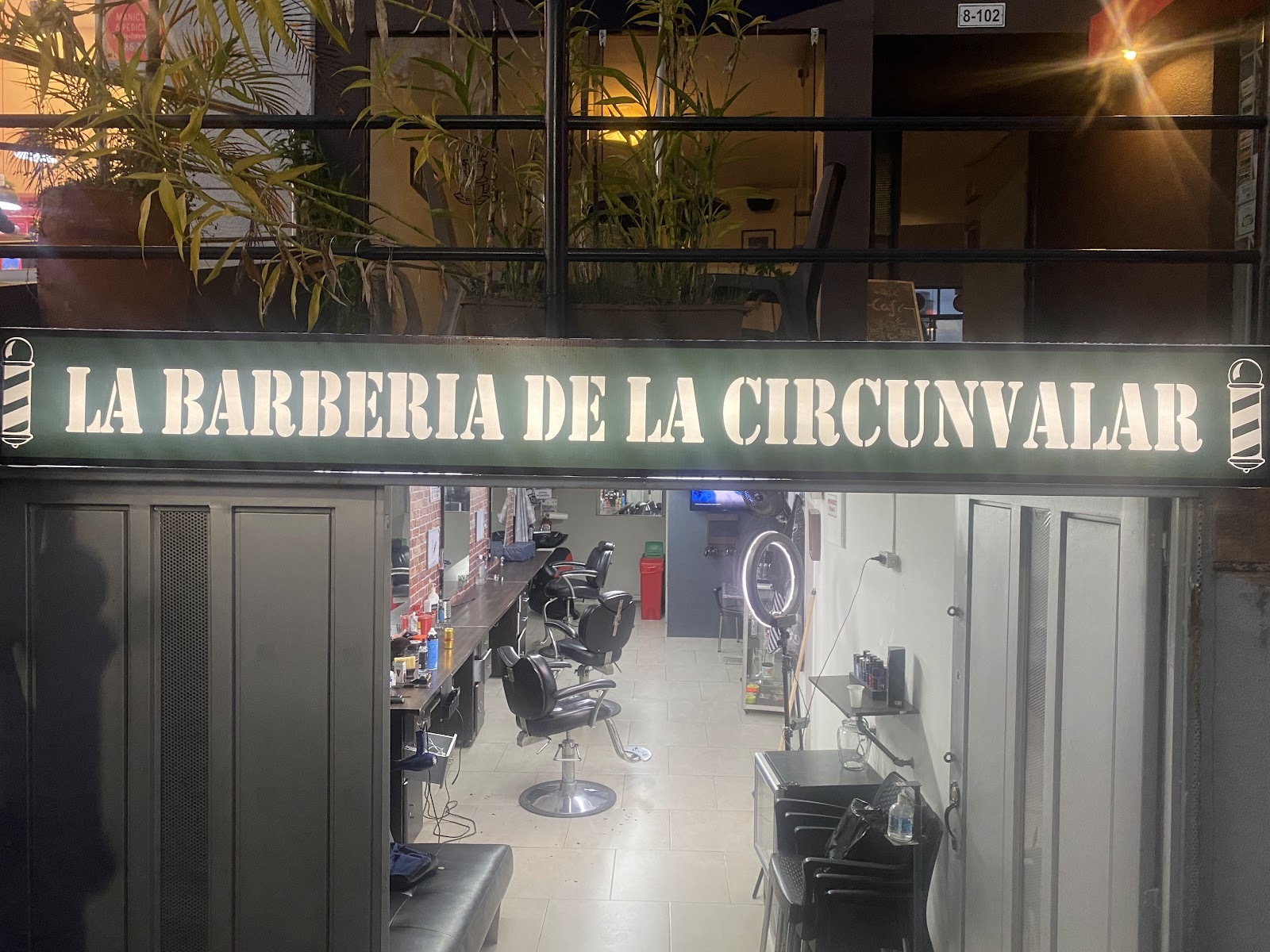 Letrero iluminado de La Barbería de la Circunvalar sobre la entrada abierta, de noche